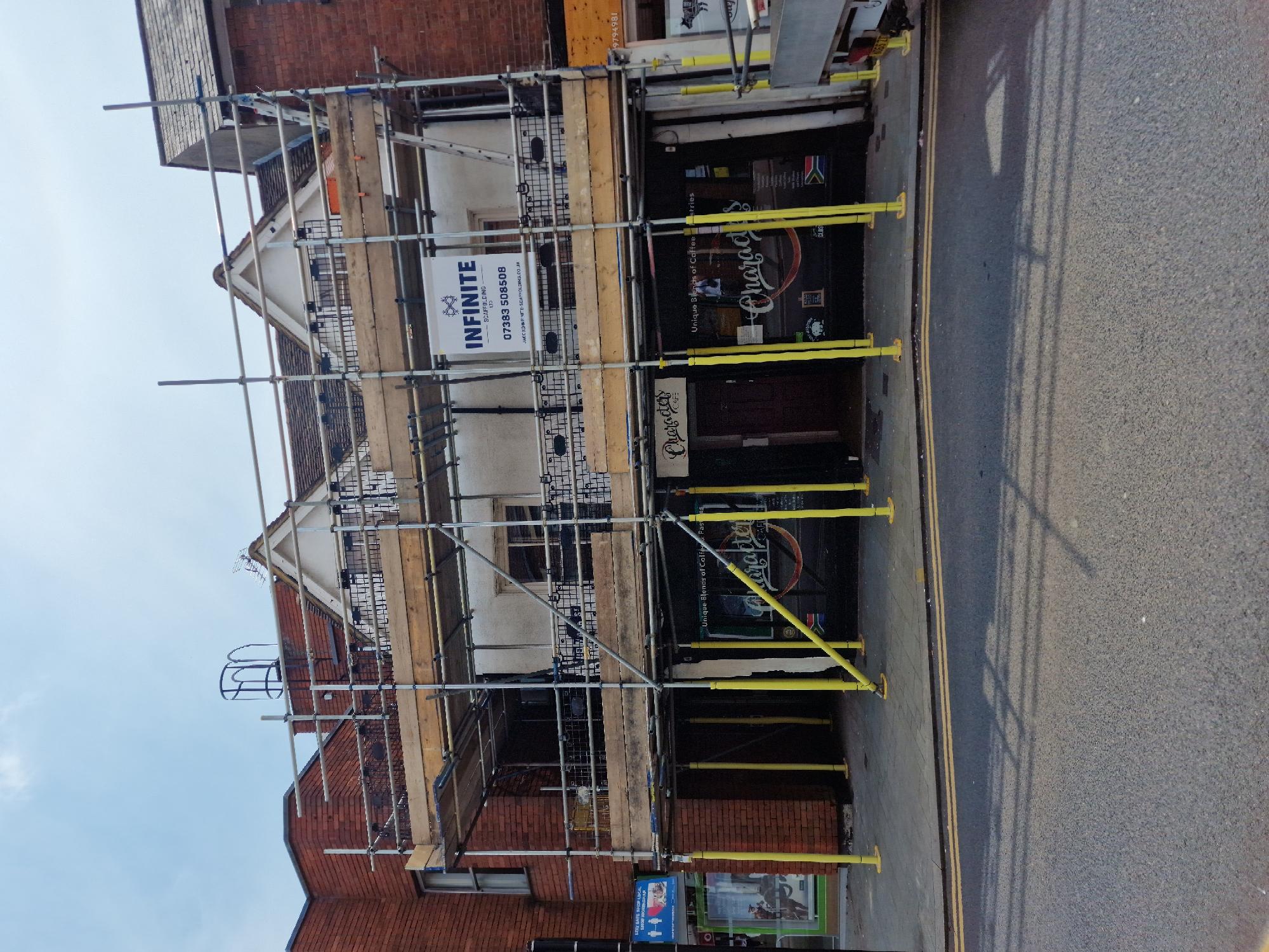 Commercial scaffold with Infinite Scaffolding site board on a high-street property